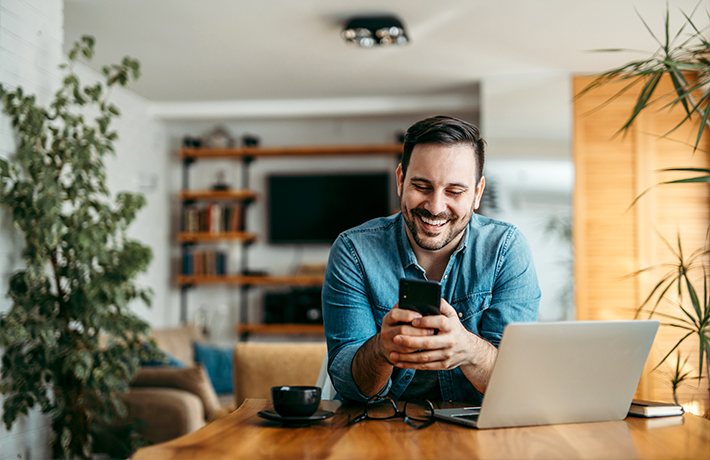 Një burrë që shikon telefonin e tij celular në shtëpi